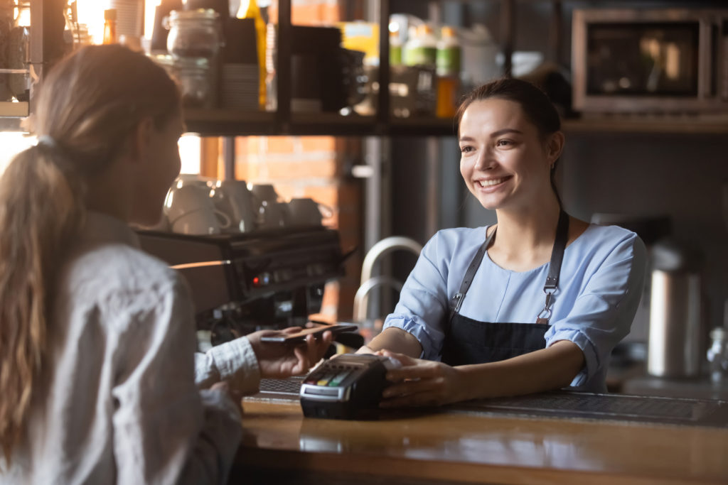 Female customer pay with phone on nfc with smiling barista