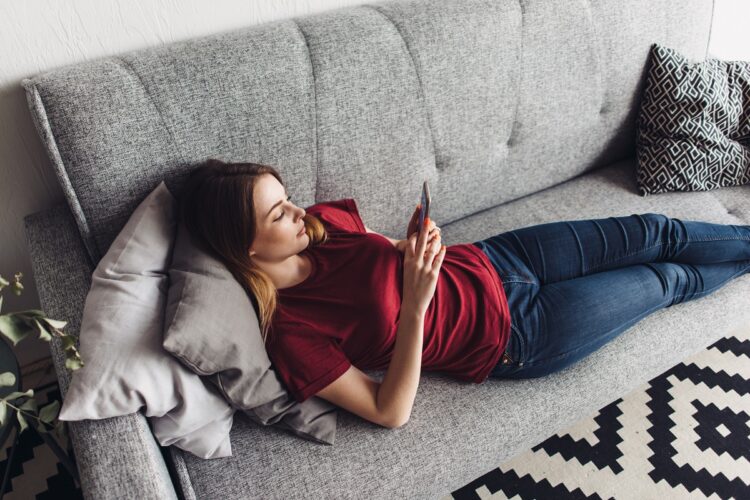 Woman lying on the sofa and using smartphone at home