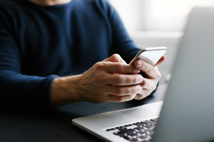 Man using mobile phone in front of laptop