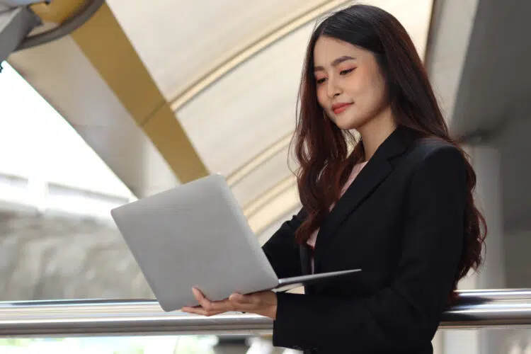 smiling young woman carrying laptop while standing