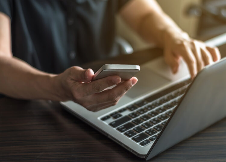 female hands working on computer while using cell phone