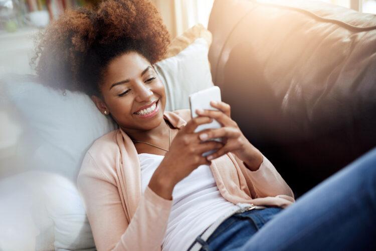 Relaxed young woman using her phone on the sofa at home.