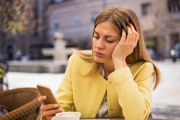 Lonely woman looking at her mobile phone while sitting at the cafe