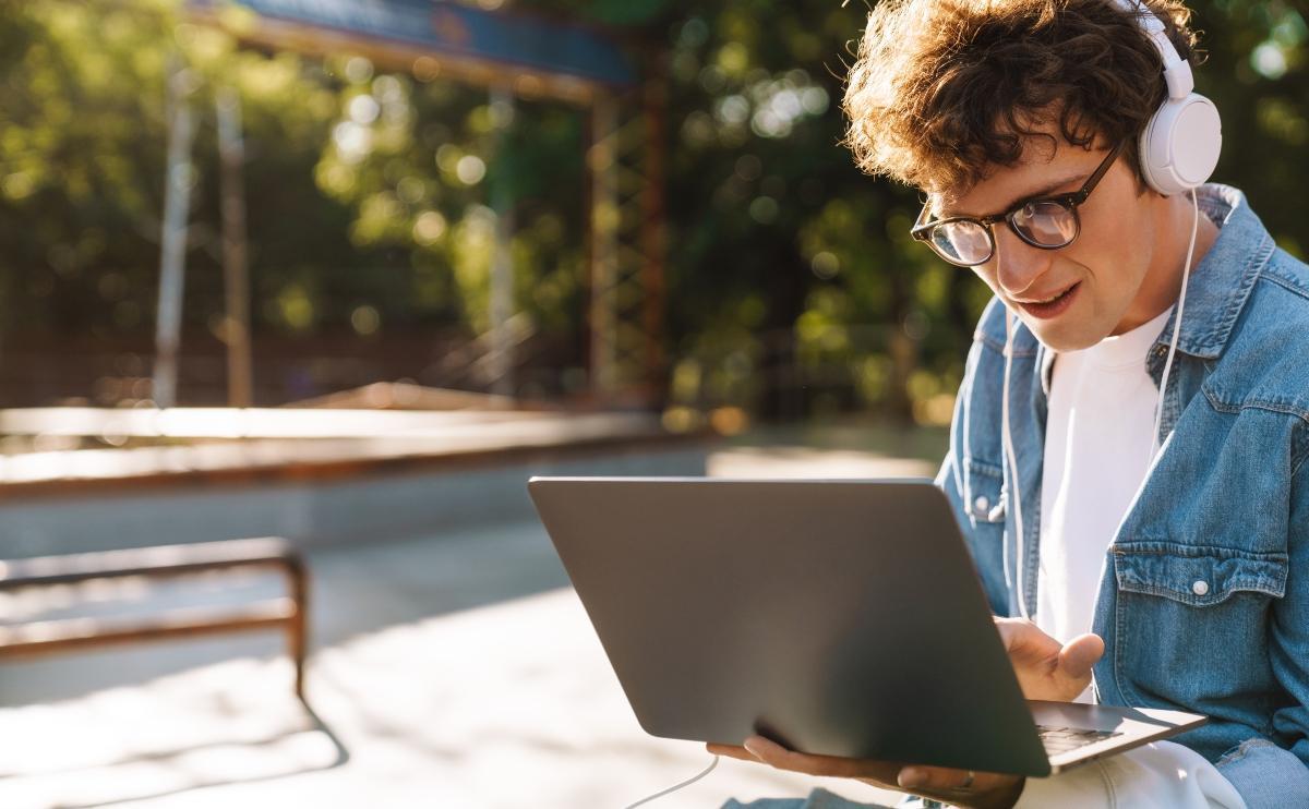 Young handsome curly boy in glasses working with laptop