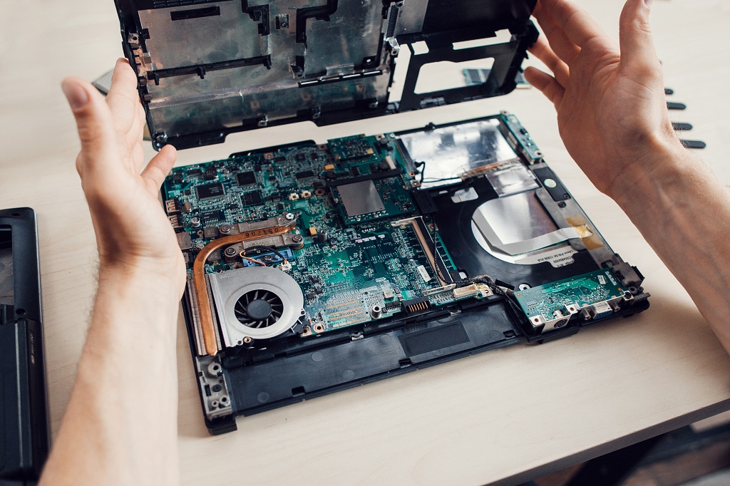 Man disassembles laptop in repair shop.