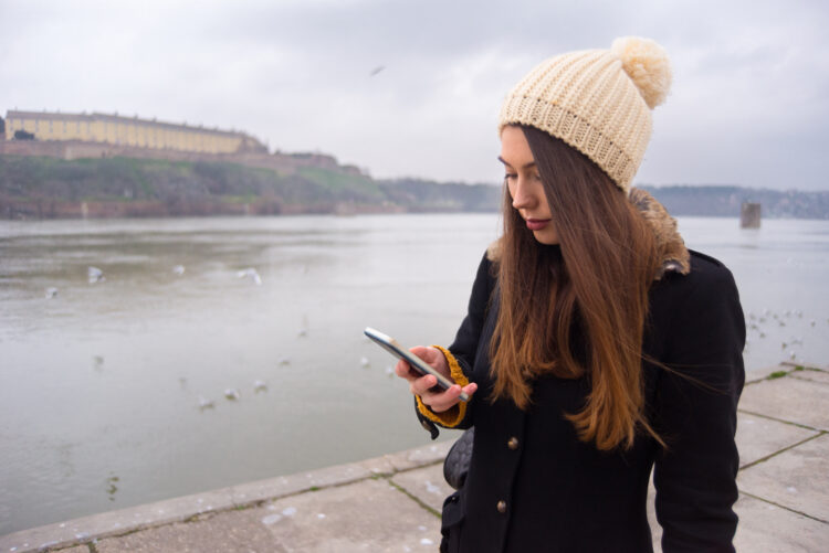 Young woman walking alone on the autumn city streets and using phone.