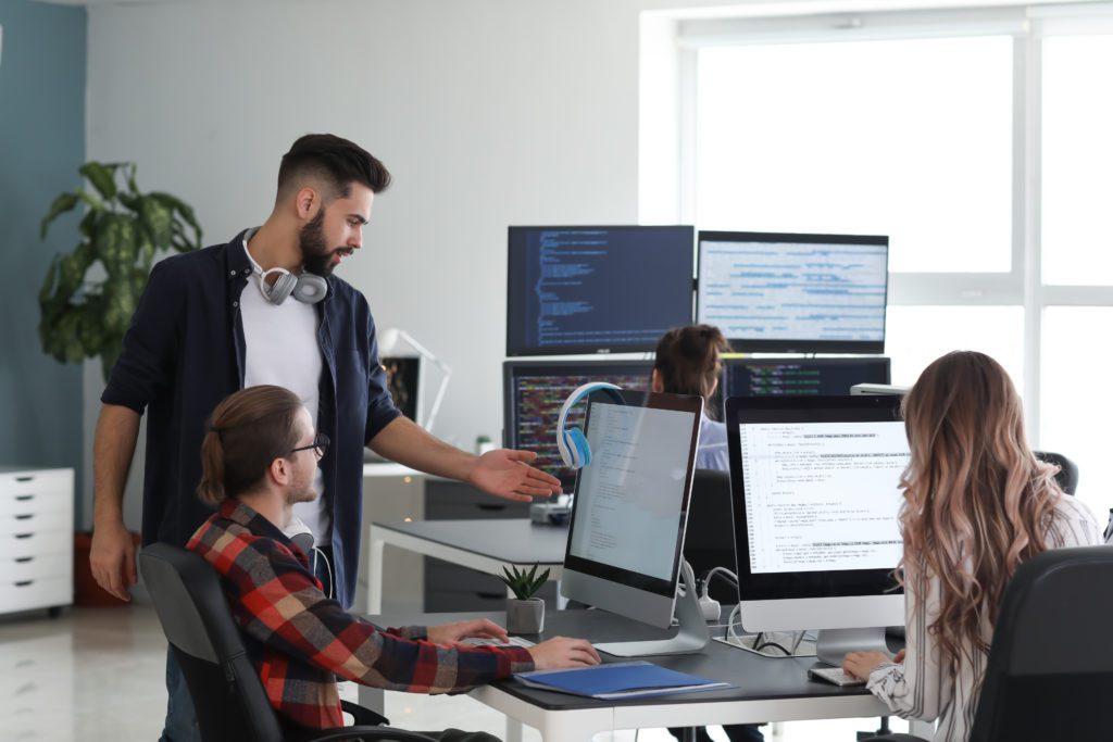 Students working with multiple computer screens inside an office learning the meaning of being an ICT manager.