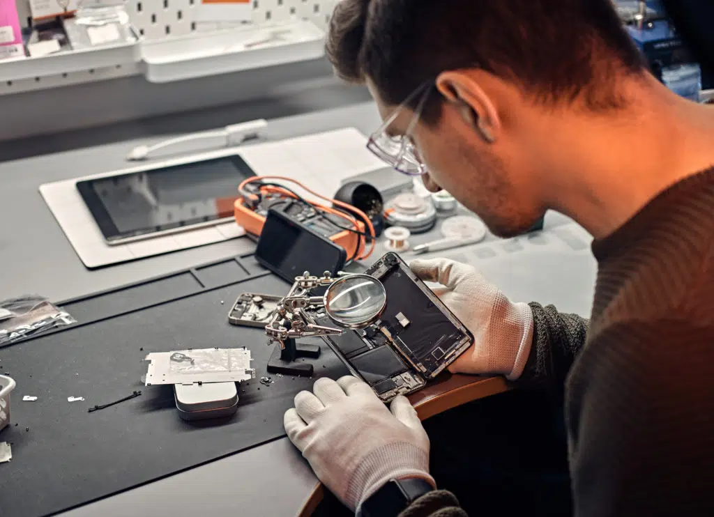 Technician inspecting smartphone parts using a magnifier.