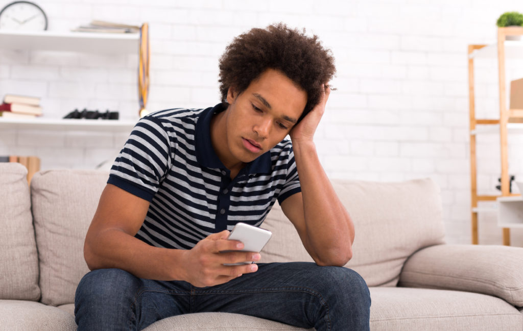 Teen guy in despair while looking at his smartphone.