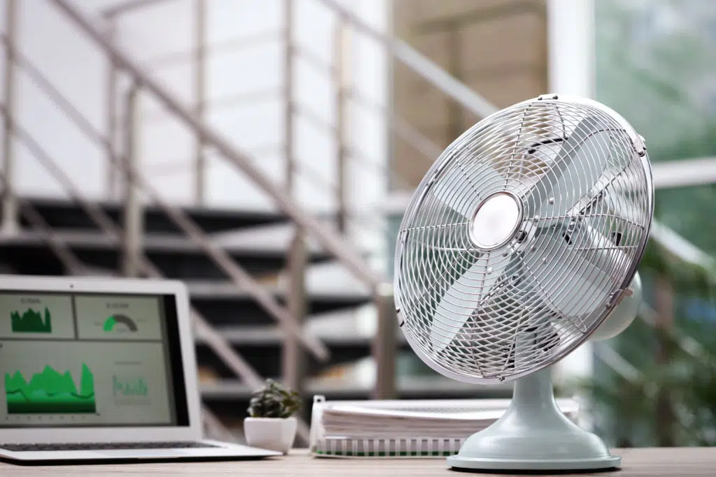 Modern electric fan on table next to the laptop in office