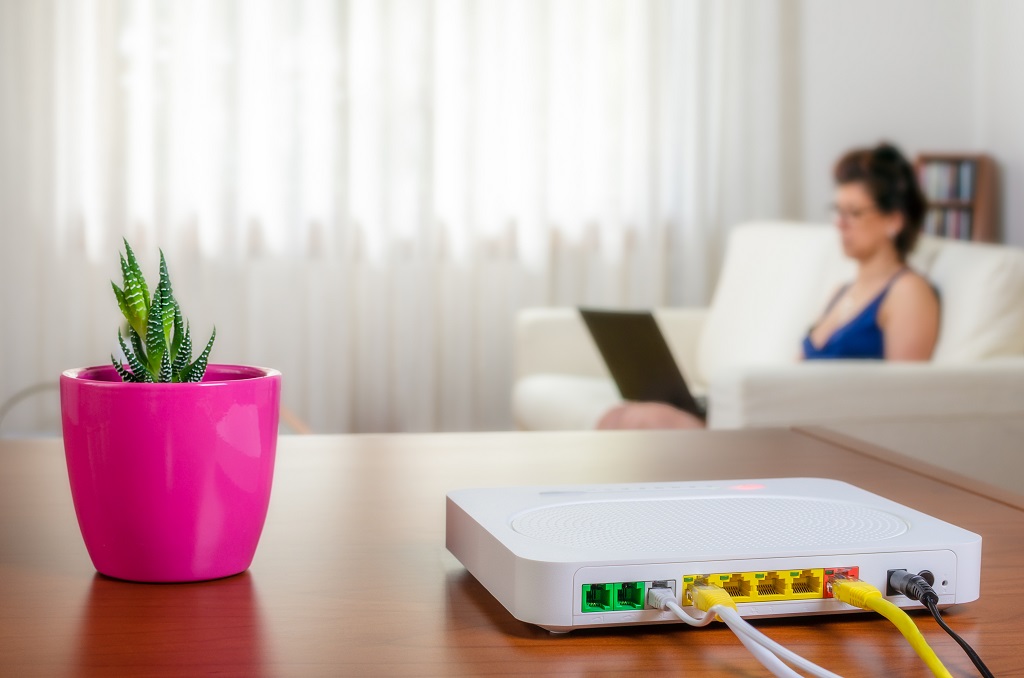 Modem router on a table in a living room and a woman using a laptop on the sofa.