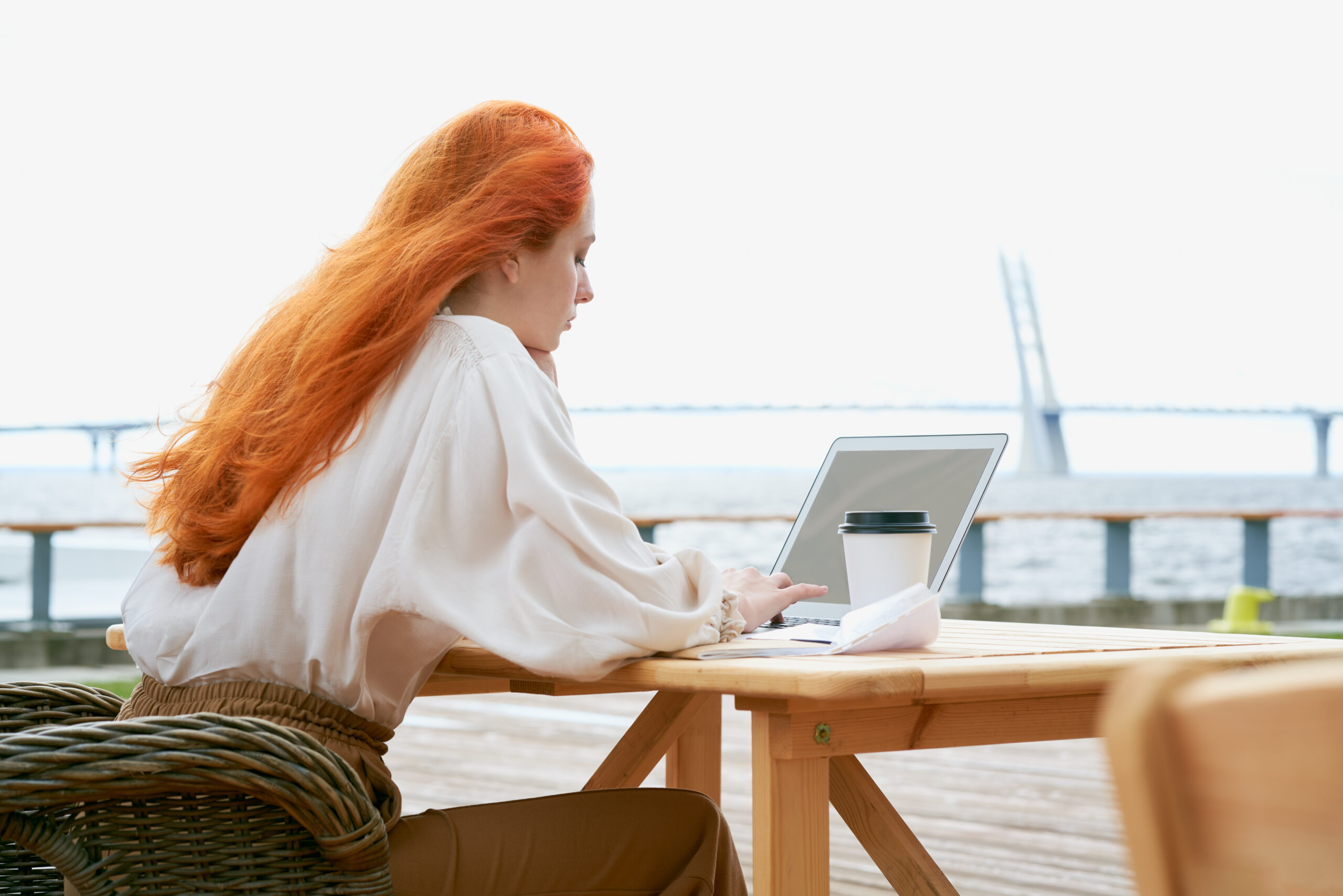 Redhead woman typing on laptop at outdoor cafe