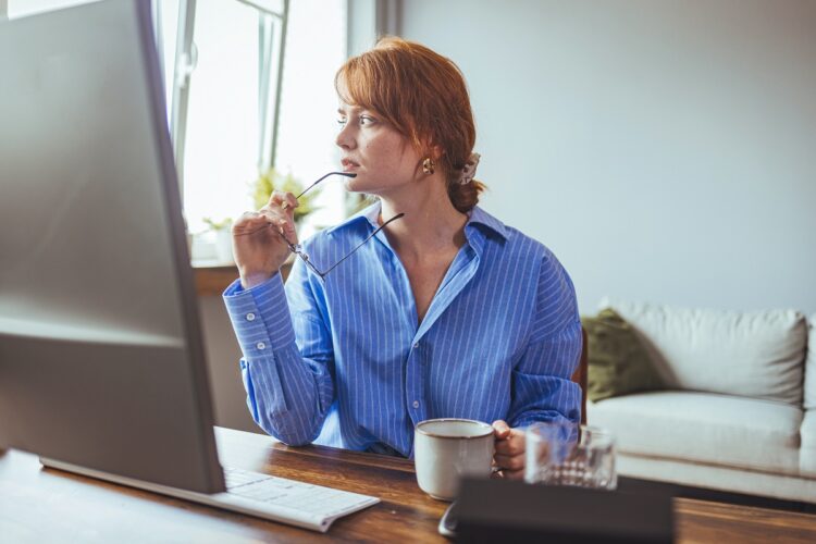 Thoughtful woman working at desktop computer looking away.