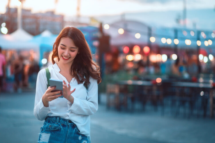 female tourist in street market smiling while using phone