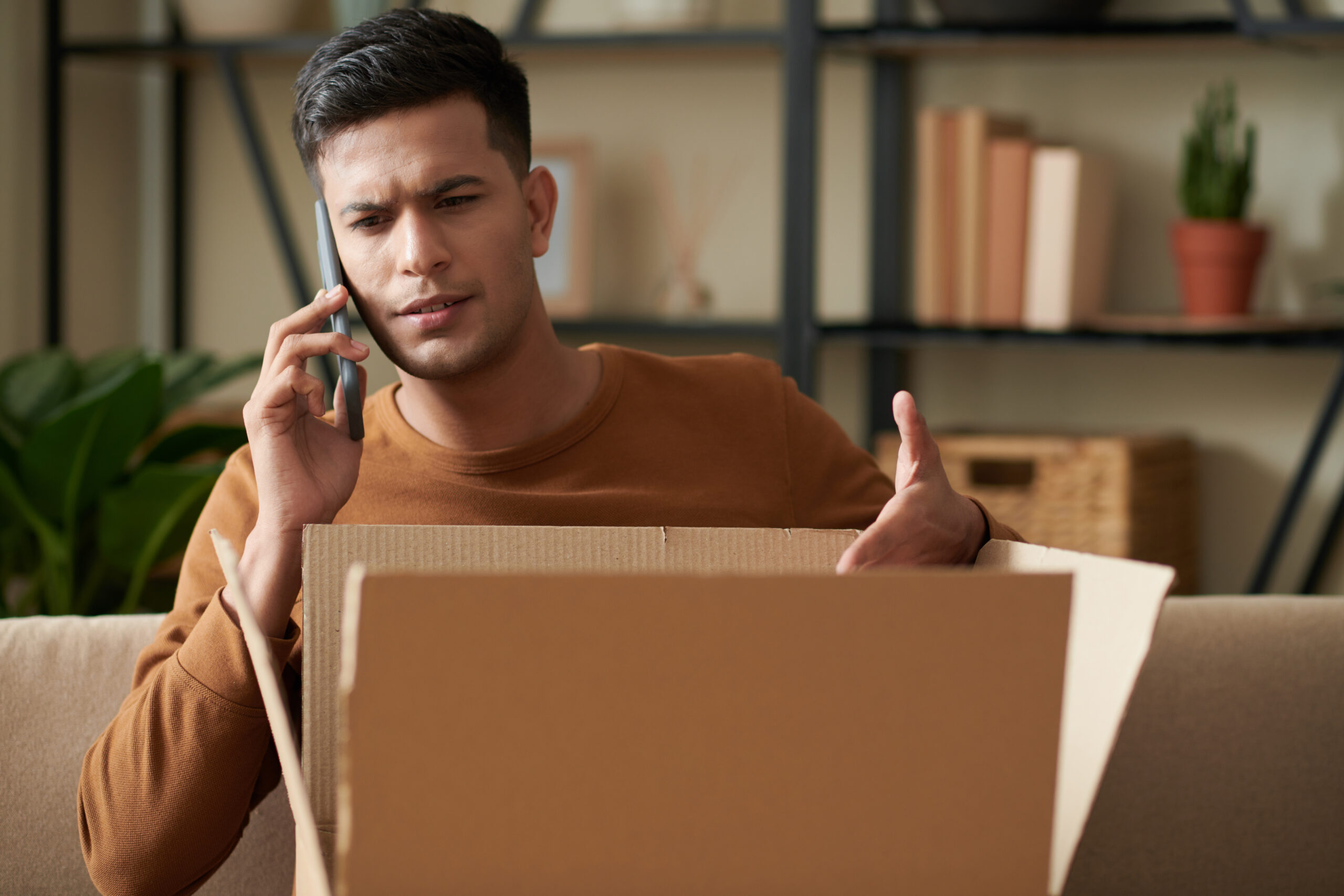 angry male customer with an opened parcel talking on the phone
