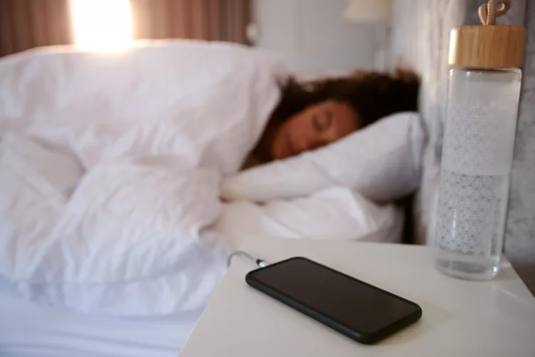 Woman asleep in bed, with mobile phone on bedside table
