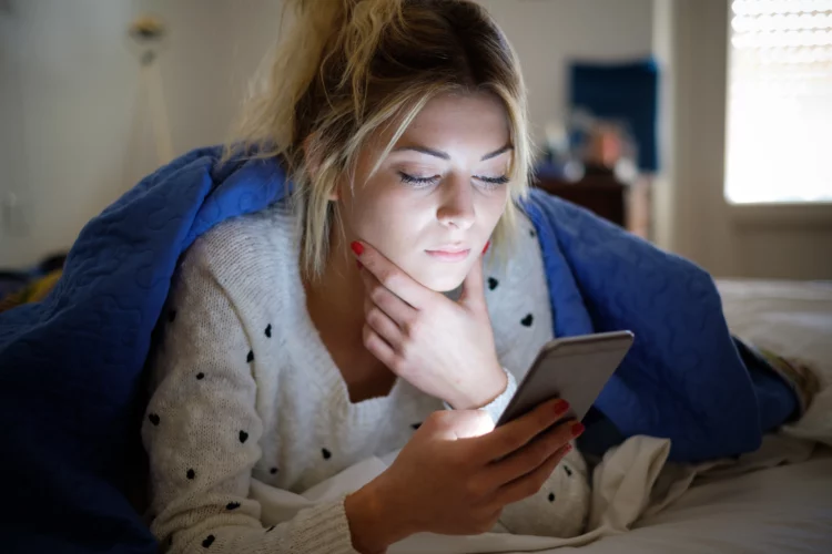 Disappointed sad woman holding mobile phone while laying on bed