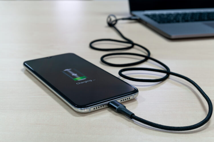 Modern smartphone is charging via the laptop on a light wooden table. 