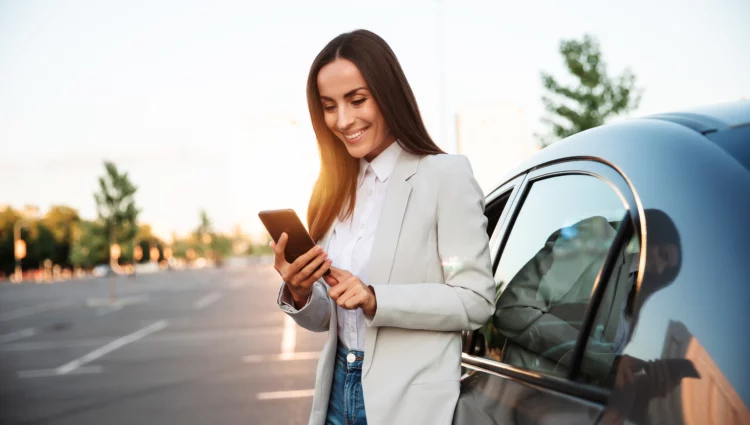 Smiling attractive woman using phone on the road by her car.