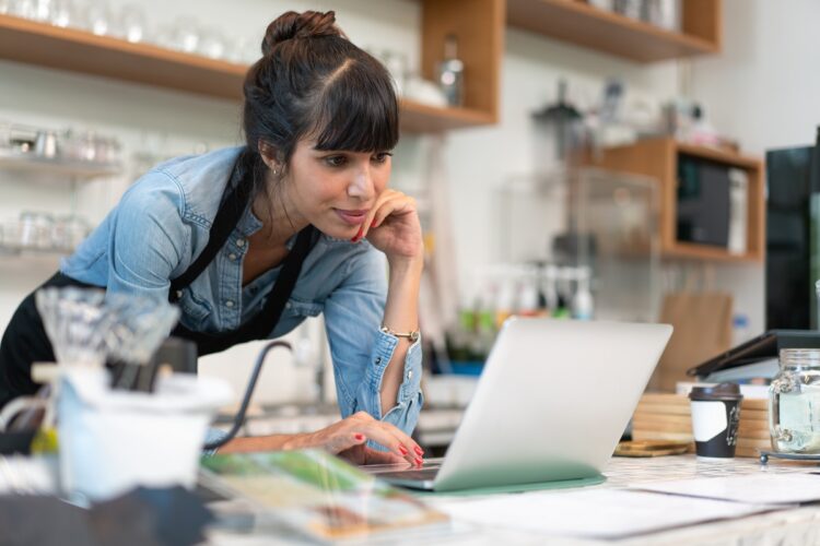 Beautiful female barista owner in apron checking online order 