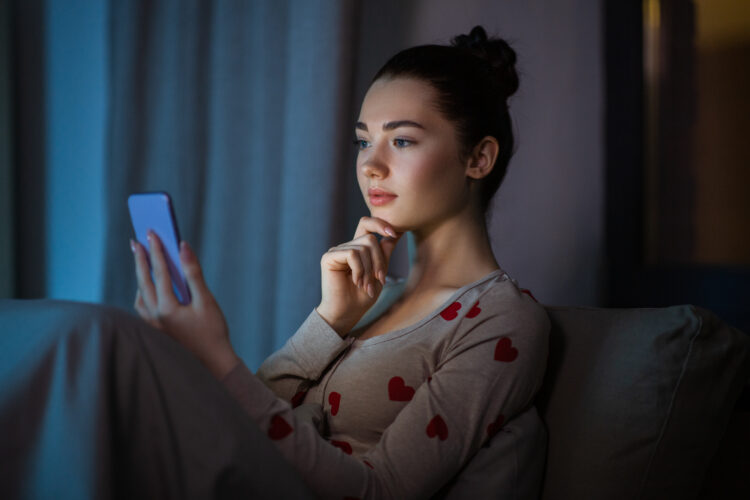 Young woman in pajamas with phone in bed at night