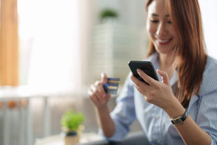 Young beautiful Asian woman using smartphone and credit card for online shopping at home.