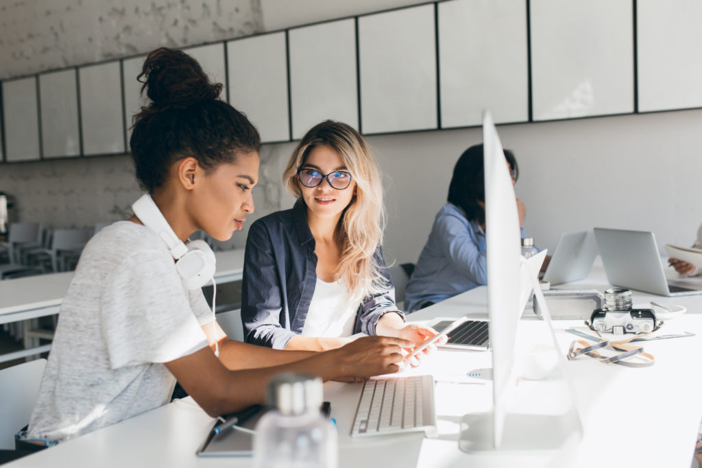 Freelance web-designer talking with friend and doing her job.