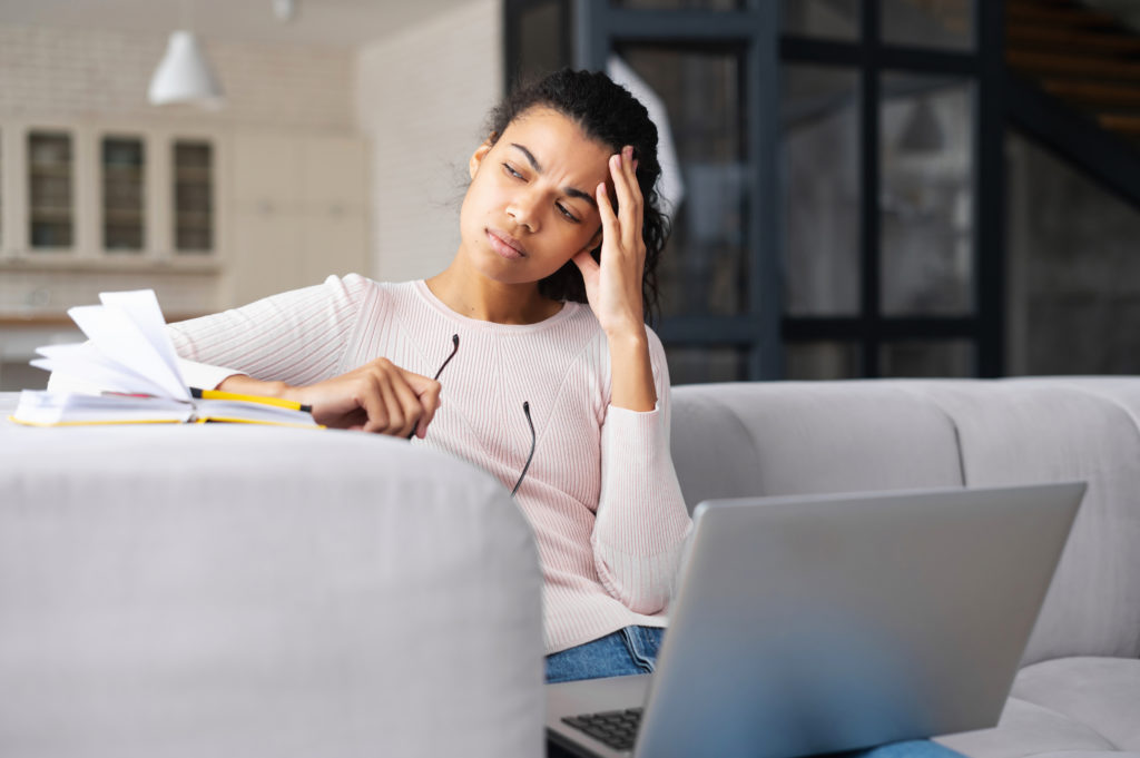 tired young woman sitting on the sofa with laptop and looking away.