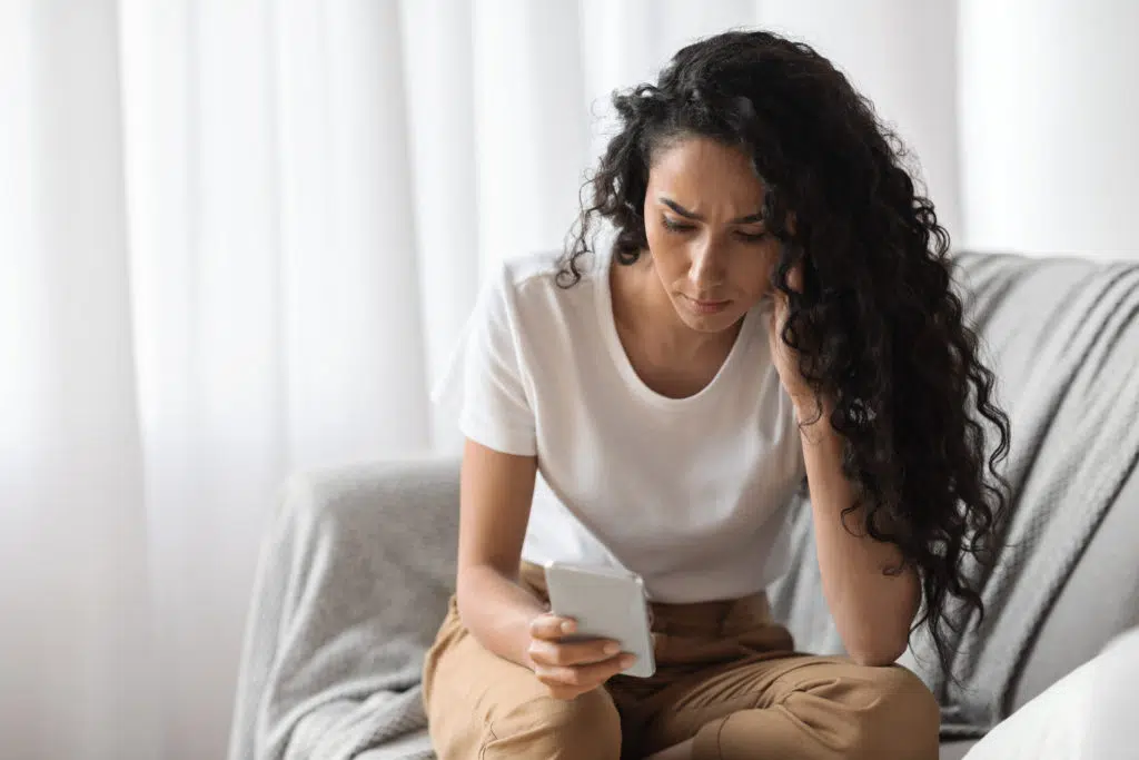 Upset woman looking at her phone at home.