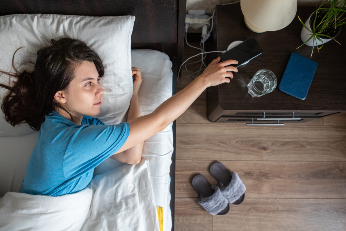 Woman taking phone from wireless charger from bedside table.