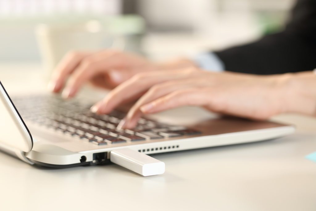 Woman using laptop with USB drive plugged in.