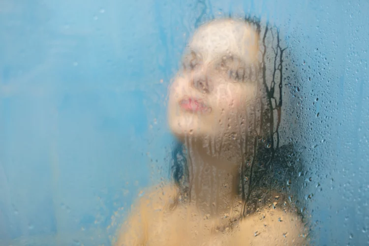 woman taking a steamy shower, glass door with water droplets