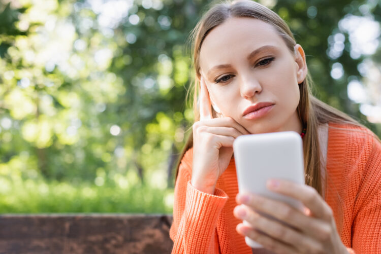 pensive woman using smartphone in park.