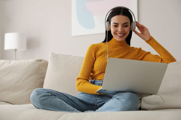 Woman with laptop and headphones sitting on sofa at home