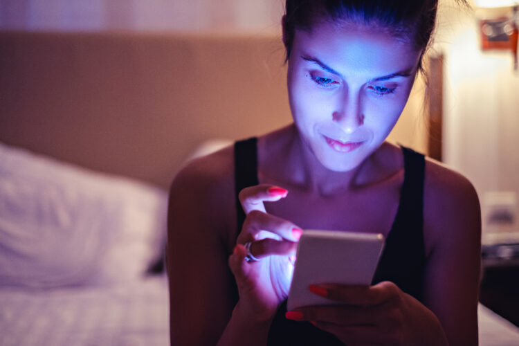 attractive young woman looking at mobile phone in the bedroom