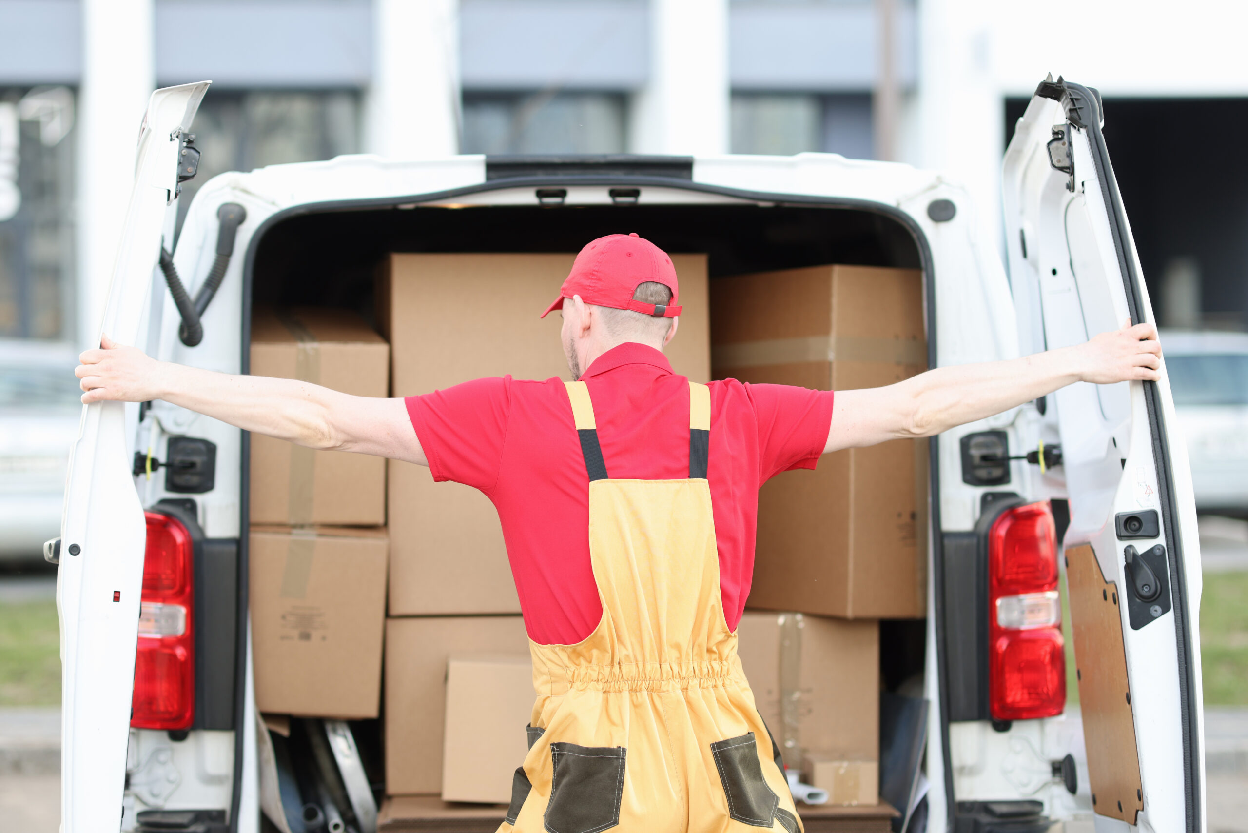 Uniformed male courier opens trunk of minivan filled with cardboard boxes