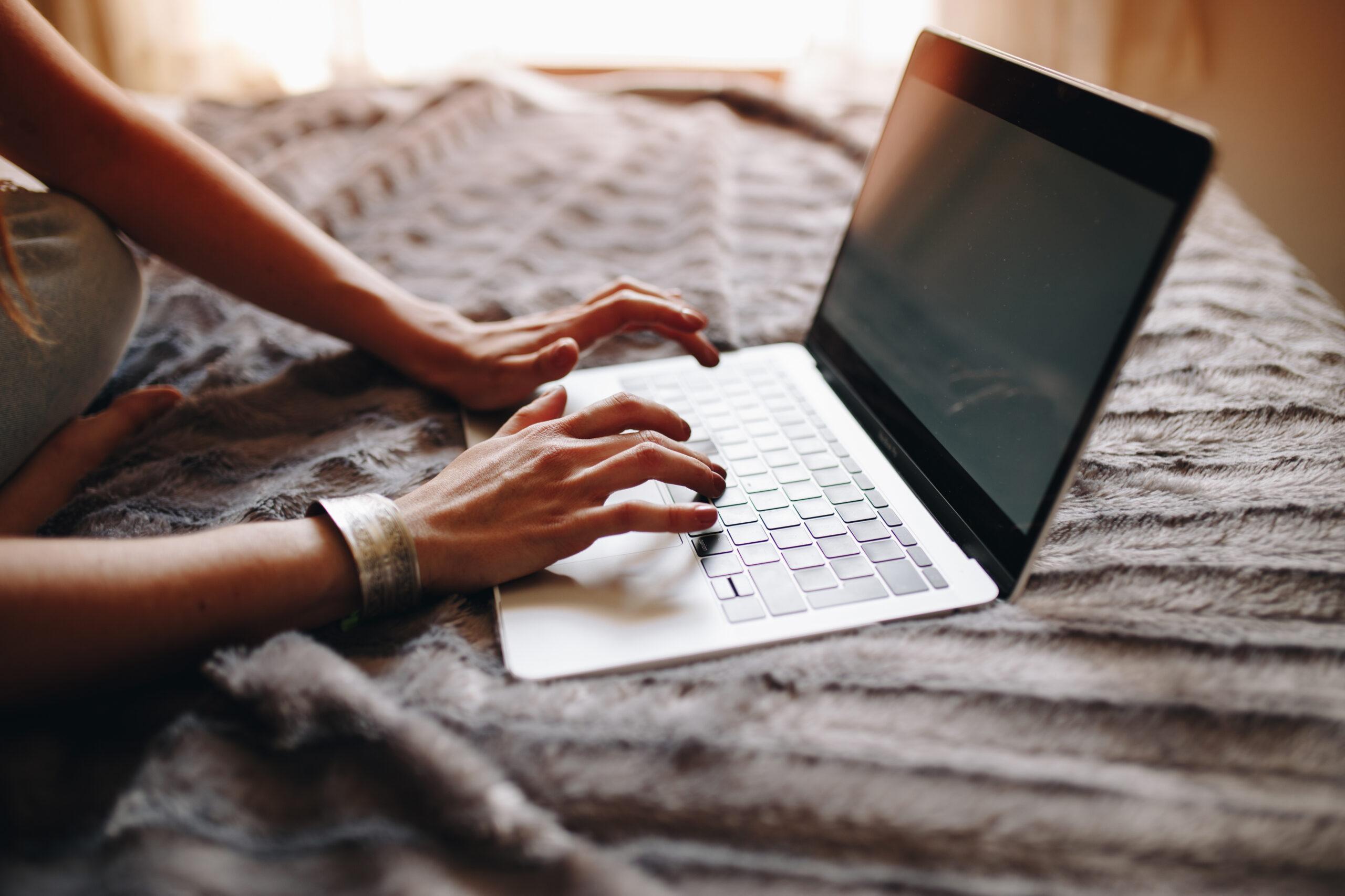 Woman's hands typing on laptop keyboard in the cozy bed. Girl us