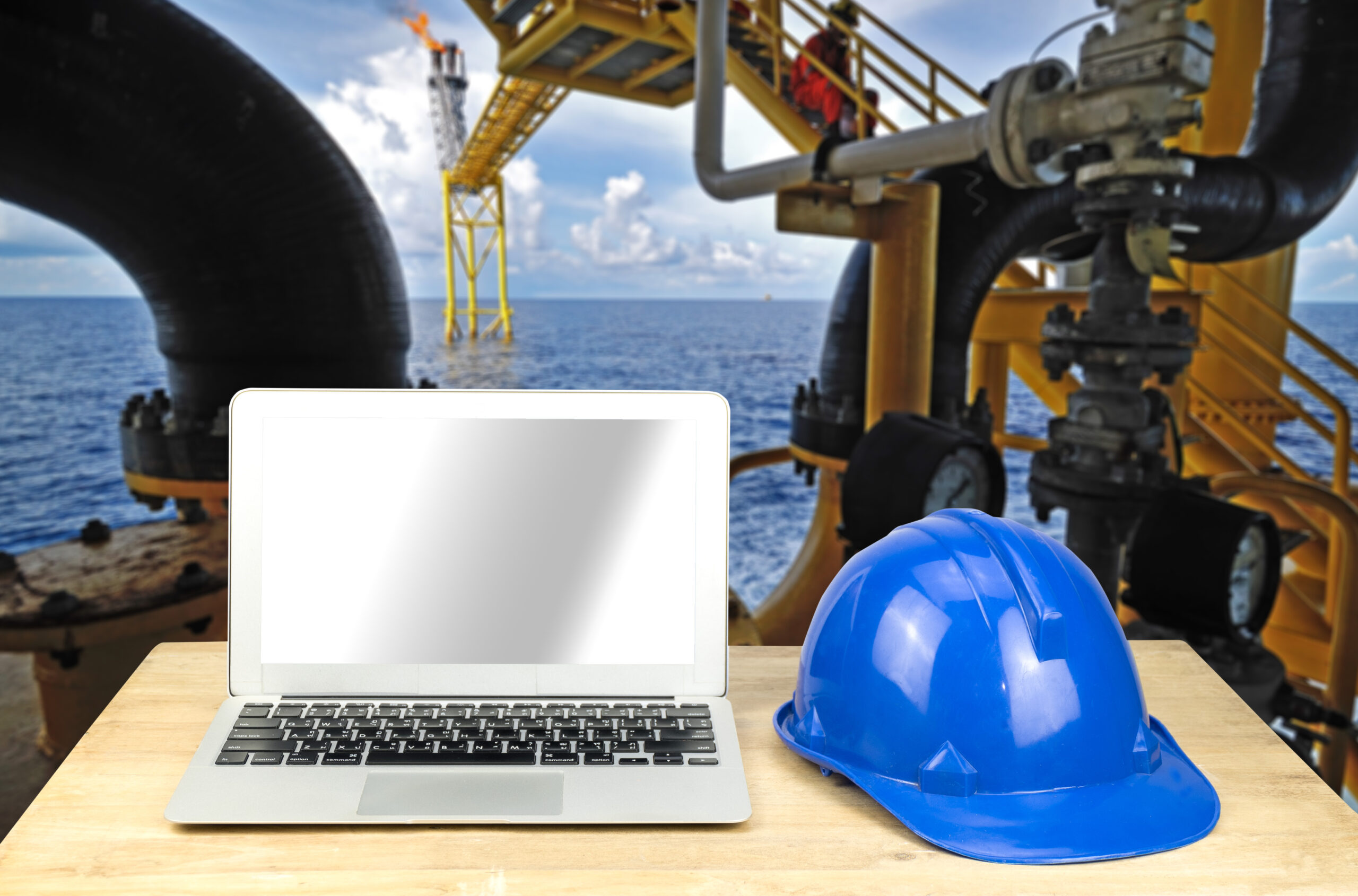 laptop and blue safety helmet on wood table at an oil rig offshore