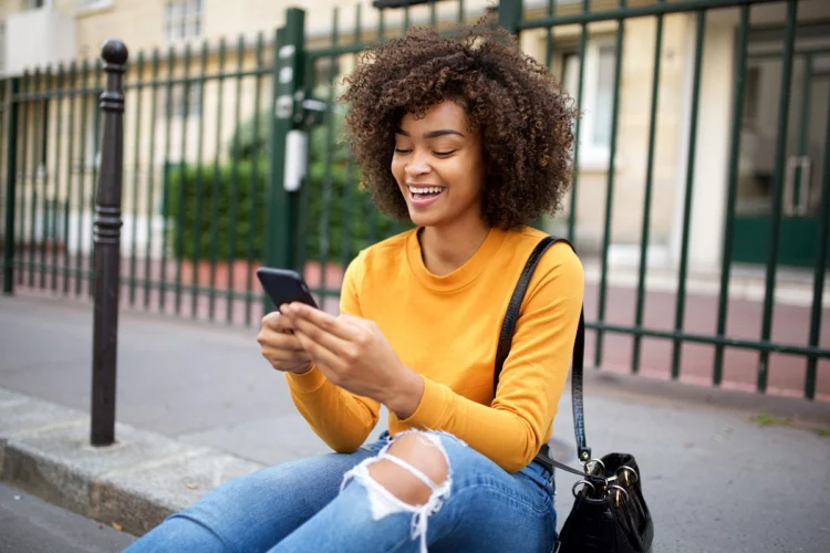 smiling young woman looking at cellphone in city