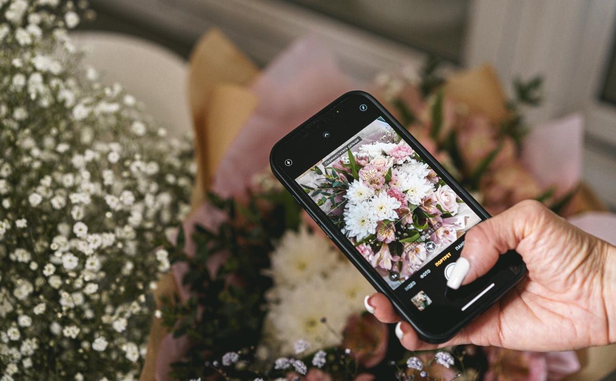 Hands holding phone and taking photo flowers flat lay