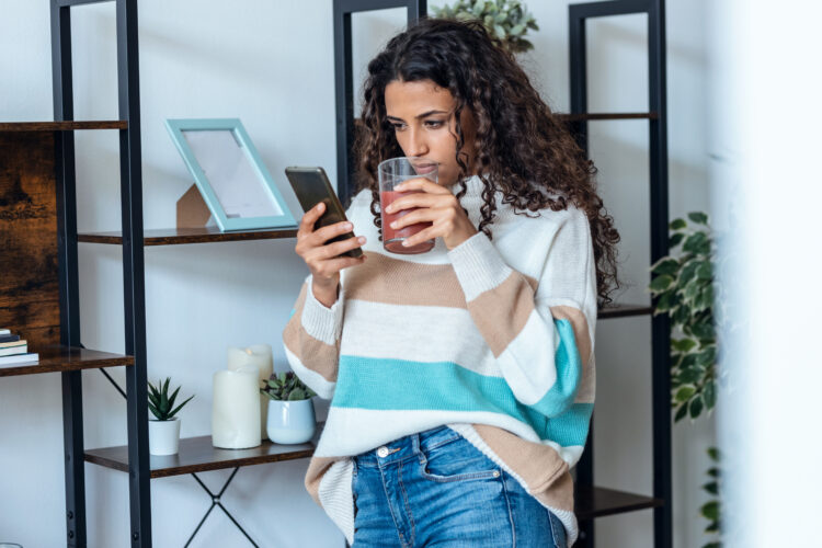 Beautiful young woman using her mobile phone while drinking detox