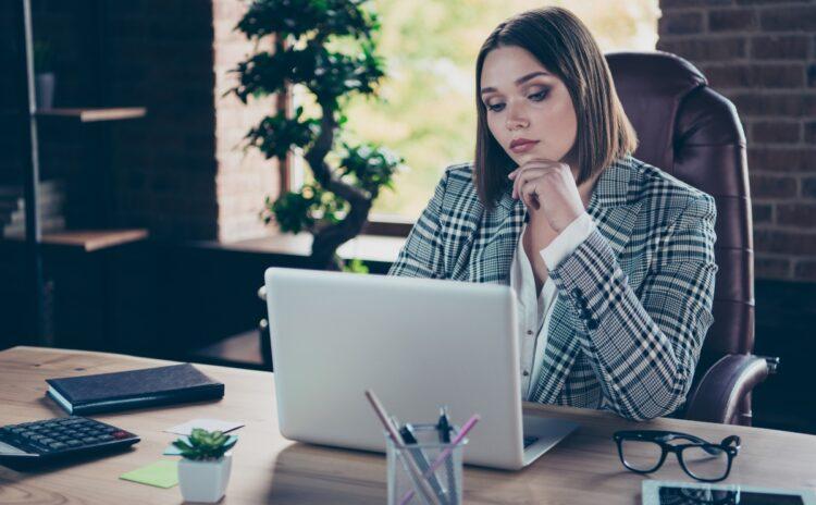 Young female executive with hand on her chin,  going through the emails in her laptop