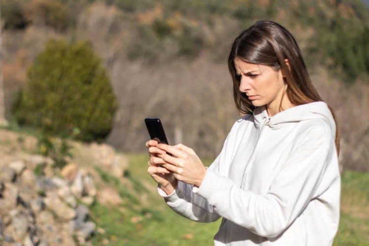 Beautiful confused brunette woman looks at smartphone outdoor.