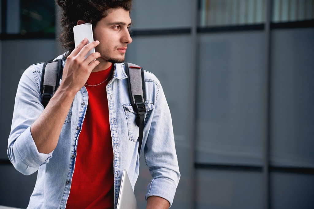 Young adult man trying to reach someone on modern smartphone on the street.