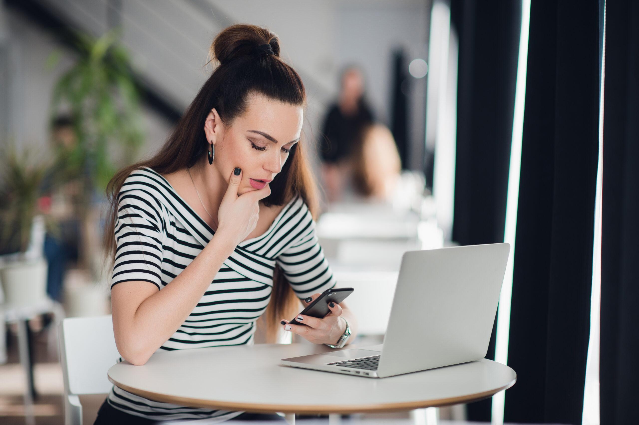 Worried woman trying to decide on an issue as she looks at her phone in a cafe