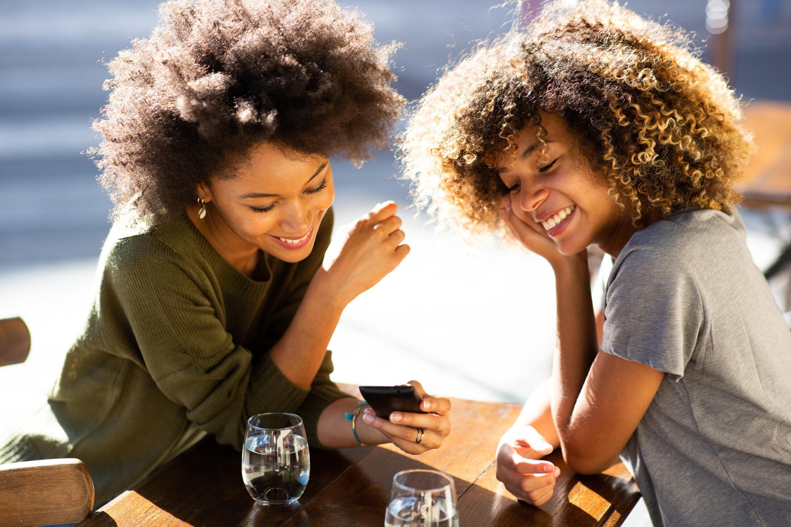 dos jóvenes afroamericanas sentadas en un café al aire libre mirando