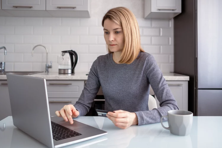 A woman sitting at a table in the kitchen with a laptop. 