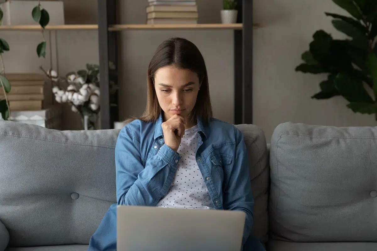 thoughtful woman sitting on the sofa looking at laptop screen