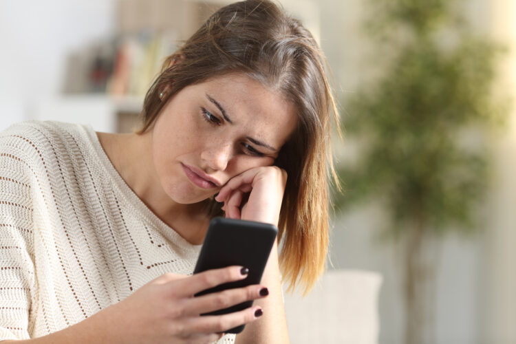 Annoyed young woman holding smart phone at home.