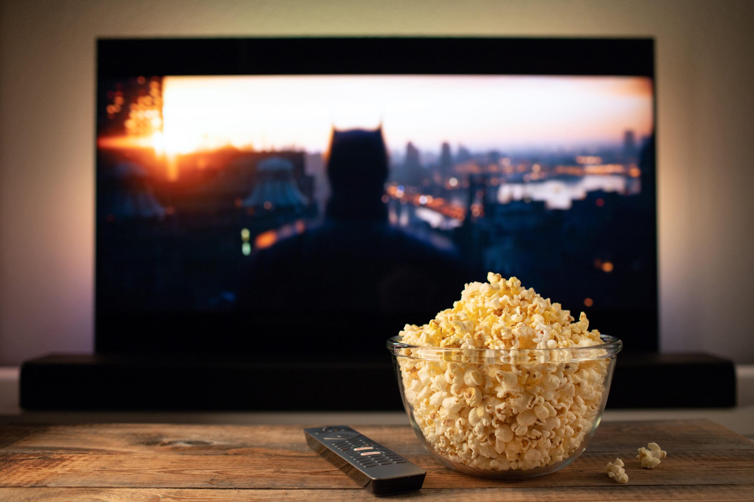 A glass bowl of popcorn and remote control in the background the TV works. Evening cozy watching a movie or TV series at home